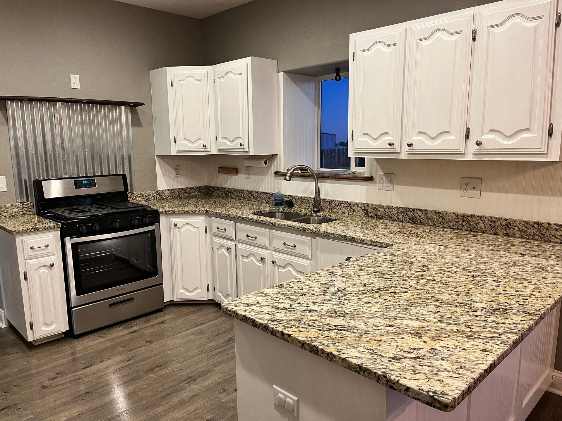 A kitchen with granite counter tops , white cabinets , a stove , and a sink.
