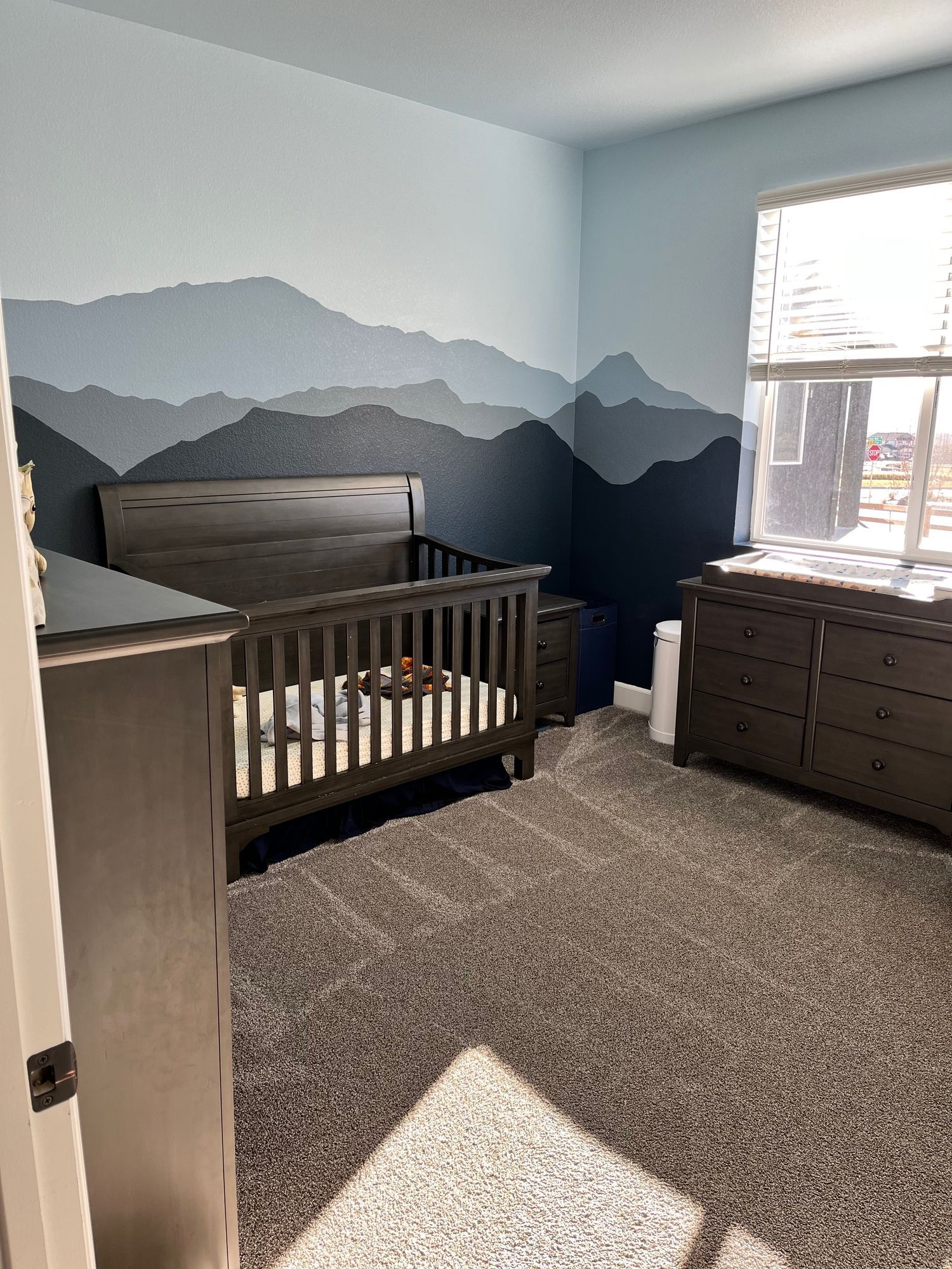 A bedroom with a crib , dresser , and window.