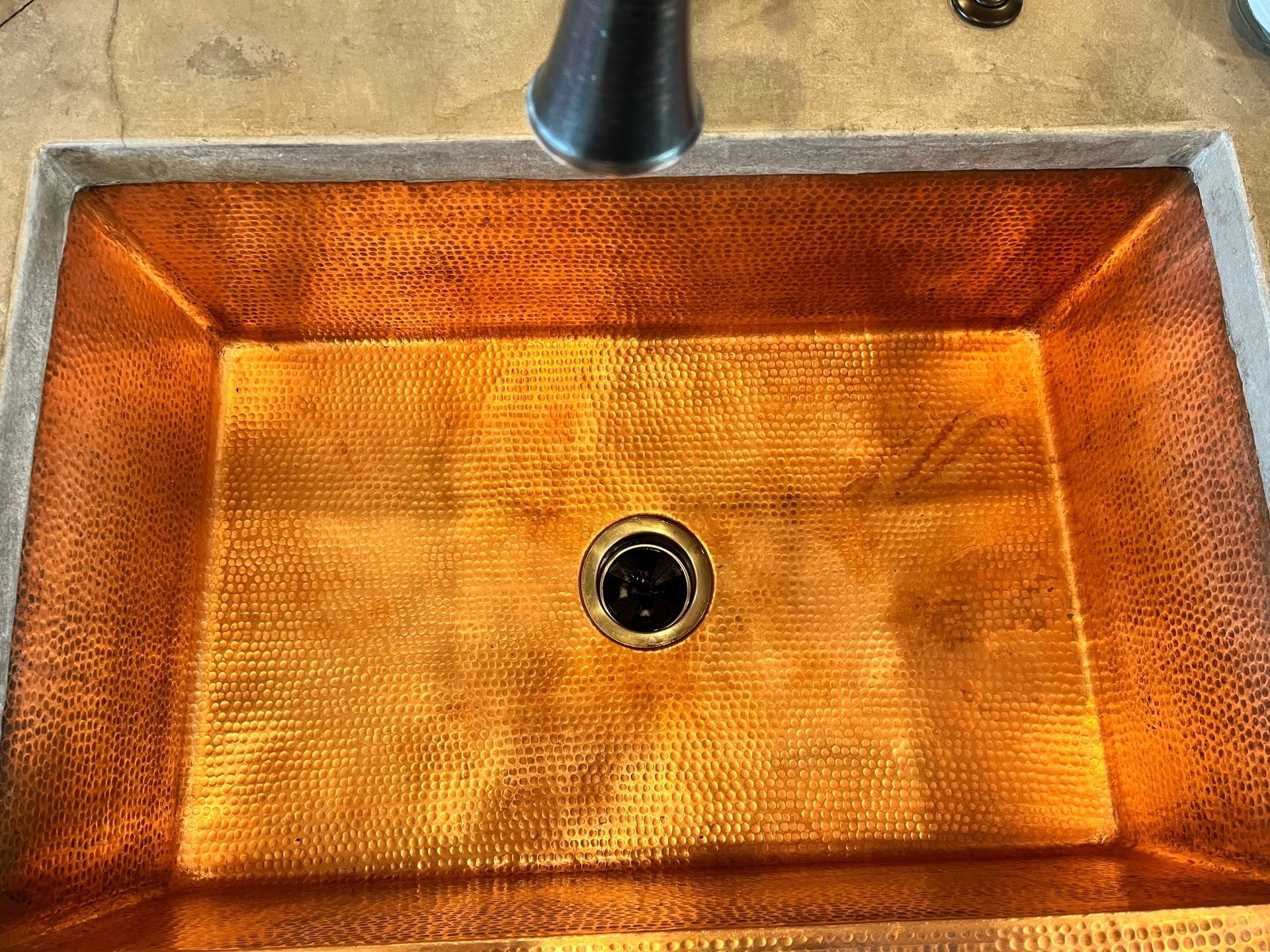 A close up of a copper sink with a black faucet