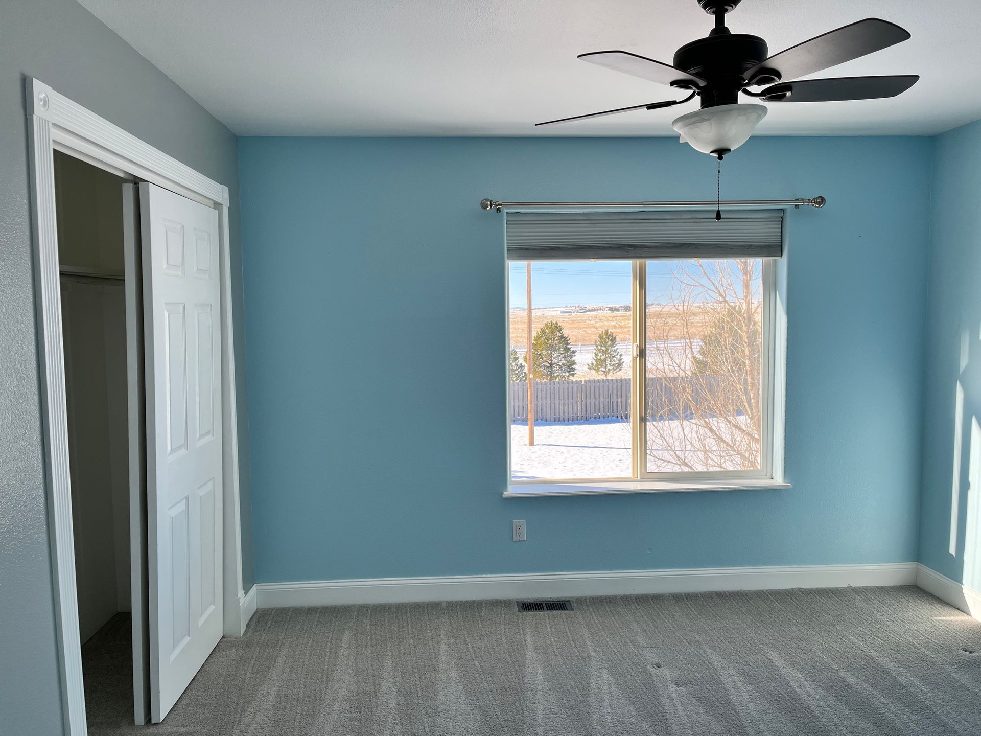 An empty bedroom with blue walls and a ceiling fan