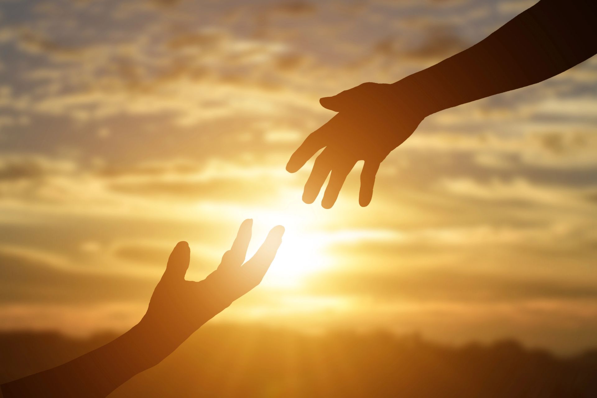 A hand reaching out to another with sunrise in the background