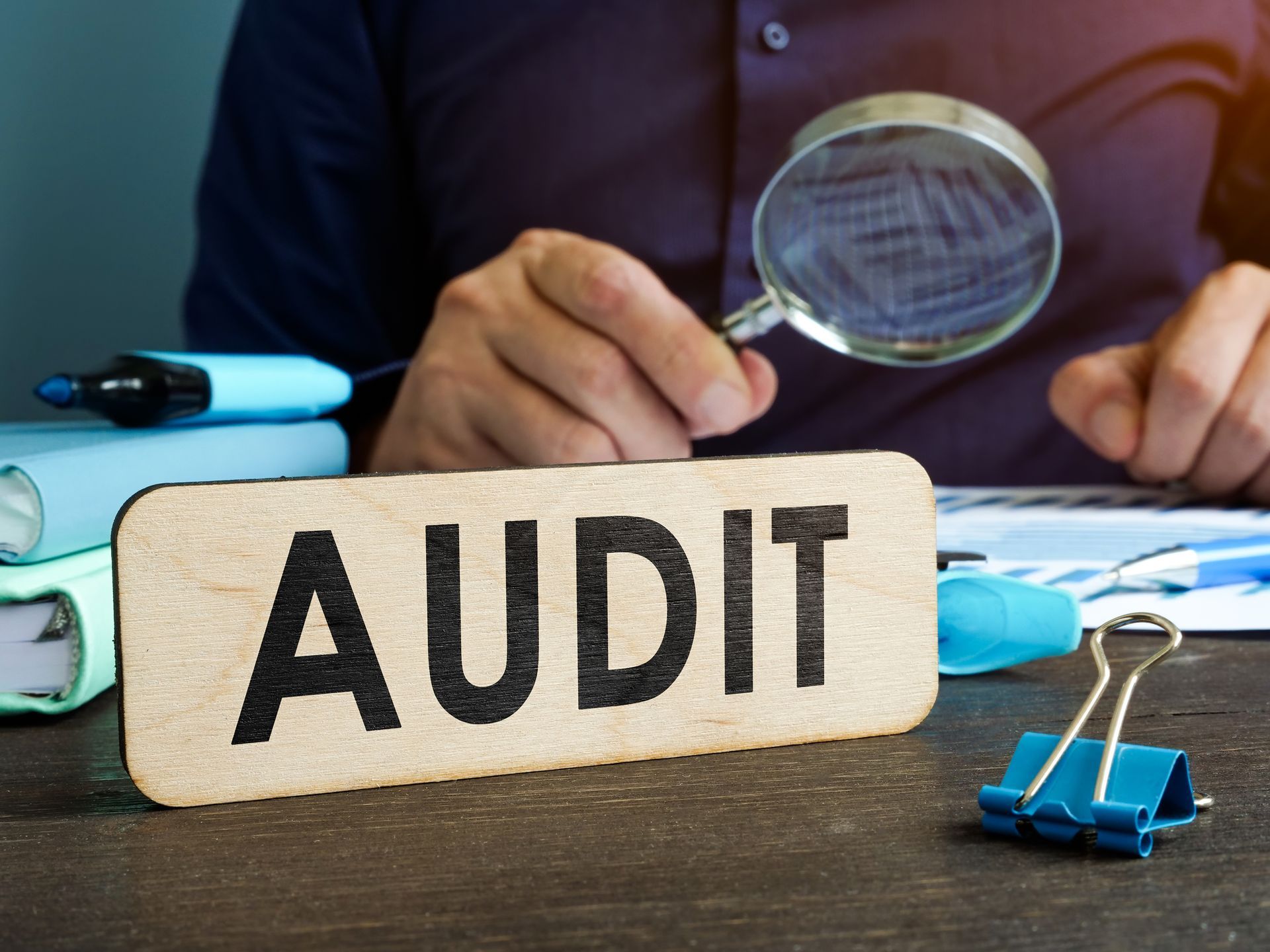 Auditor with a magnifying glass looking at papers on a desk