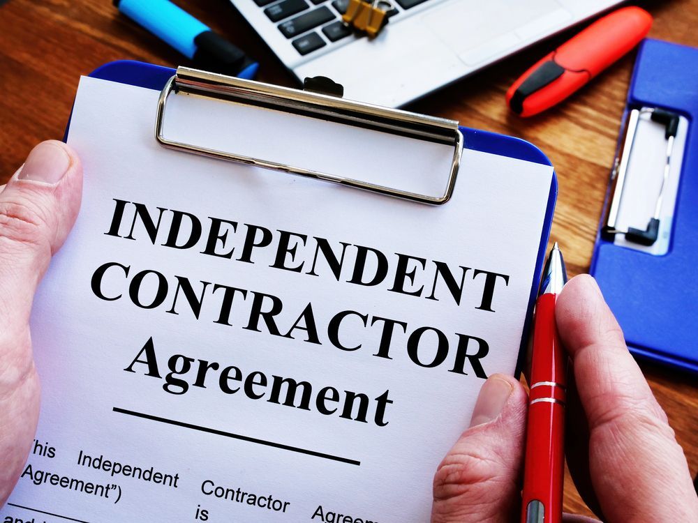 Independent contract agreement on a clipboard and a red pen held by a man’s hand