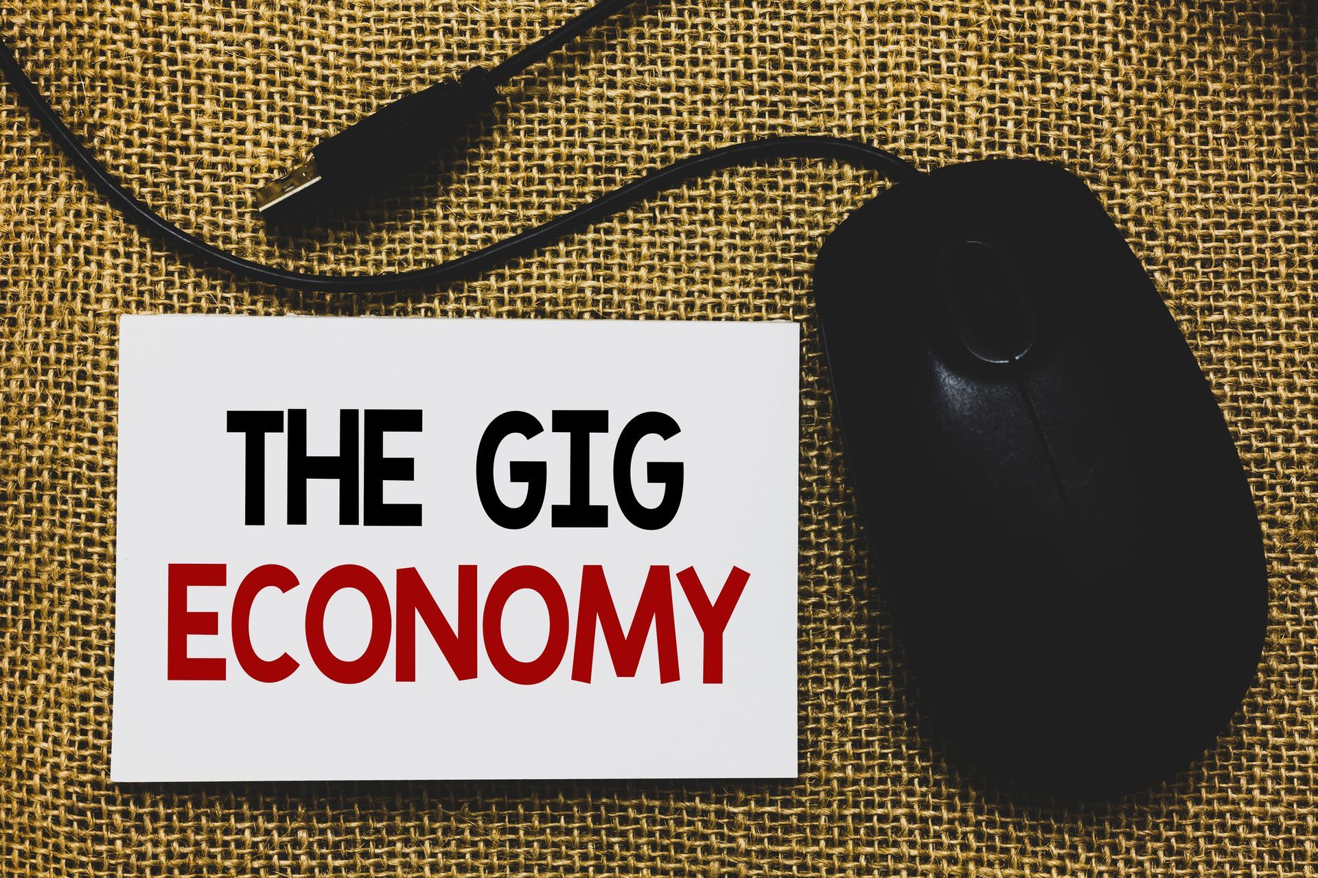 Sign saying THE GIG ECONOMY lying on a desk next to a computer mouse