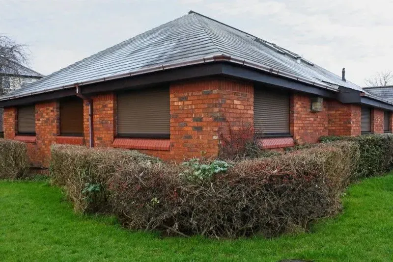 A brick building with a roof and a hedge in front of it  — LT Shutters in Sussex, NSW