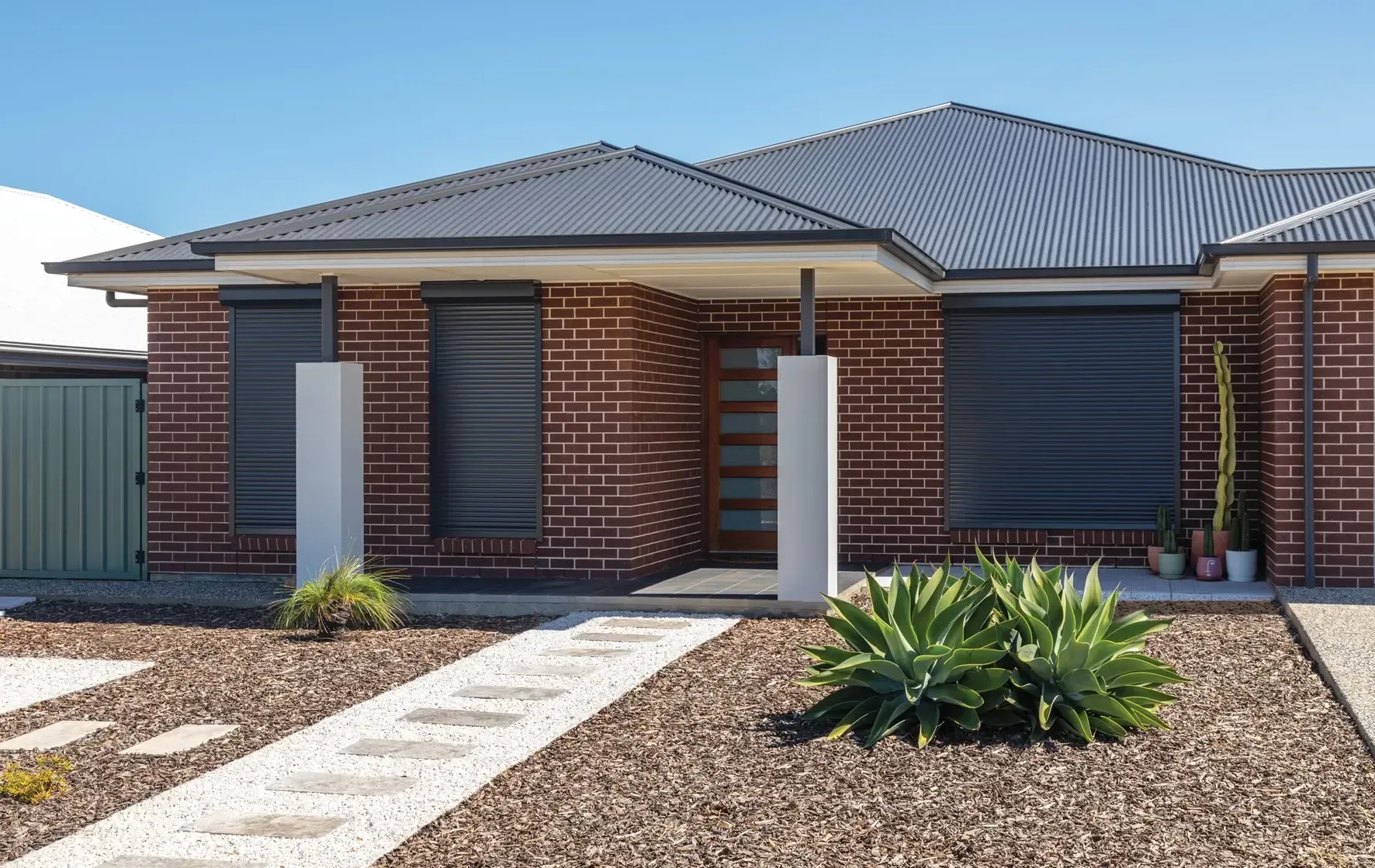 A brick house with a black roof and shutters on the windows — LT Shutters in Jervis Bay, NSW