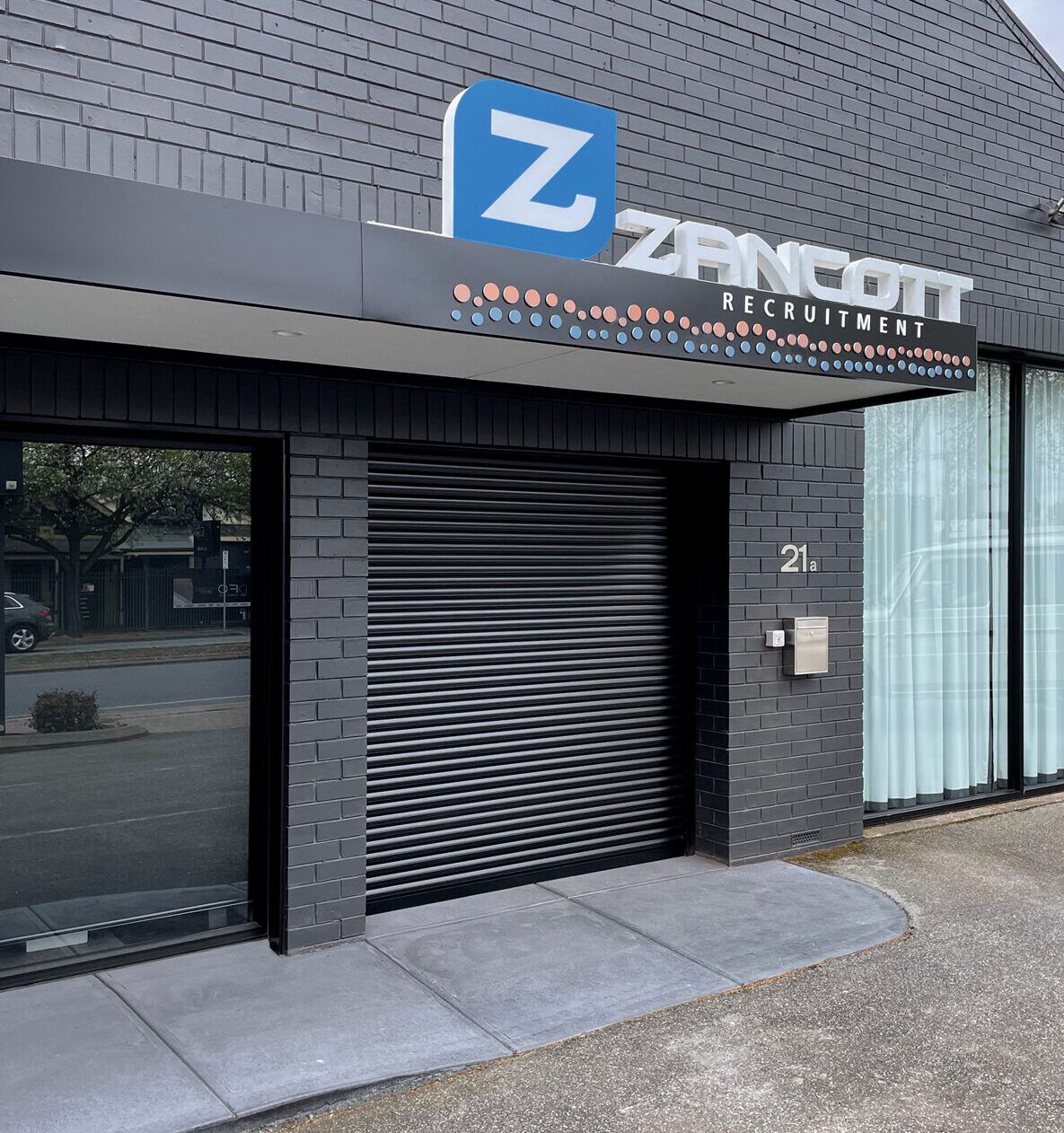 A brick building with a sign that says Zancott — LT Shutters in Bellambi, NSW
