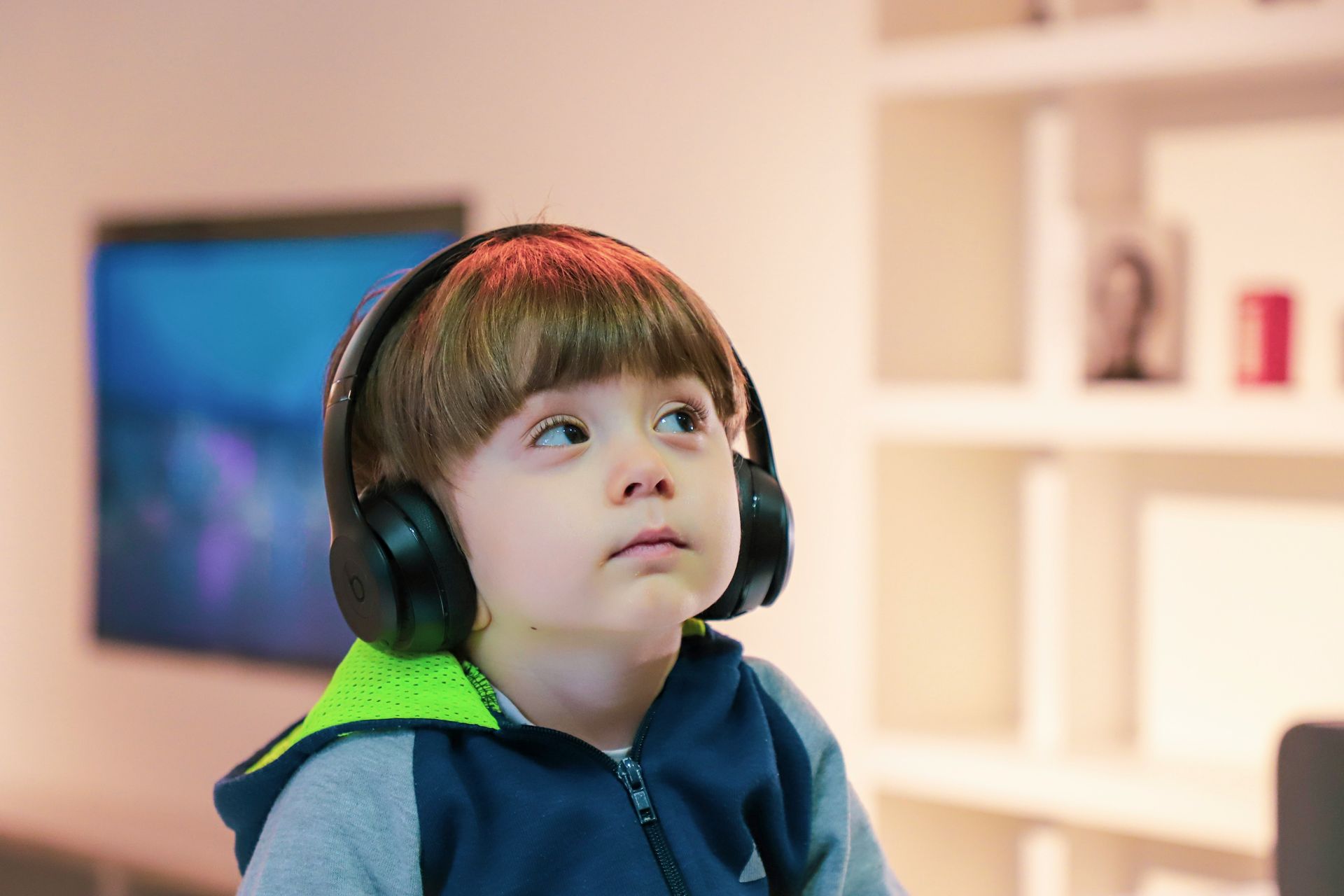 A young boy wearing headphones is looking up in a living room.