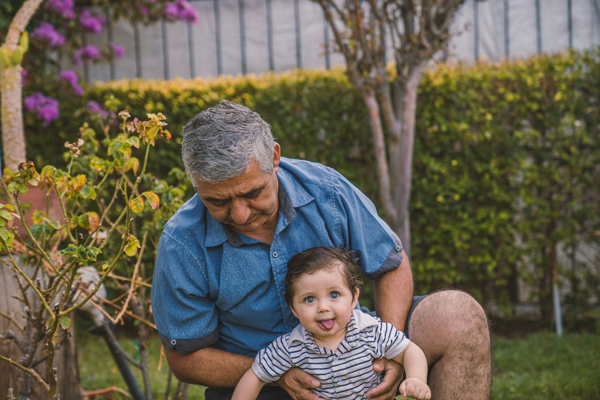 A man is holding a baby in his lap in a garden.