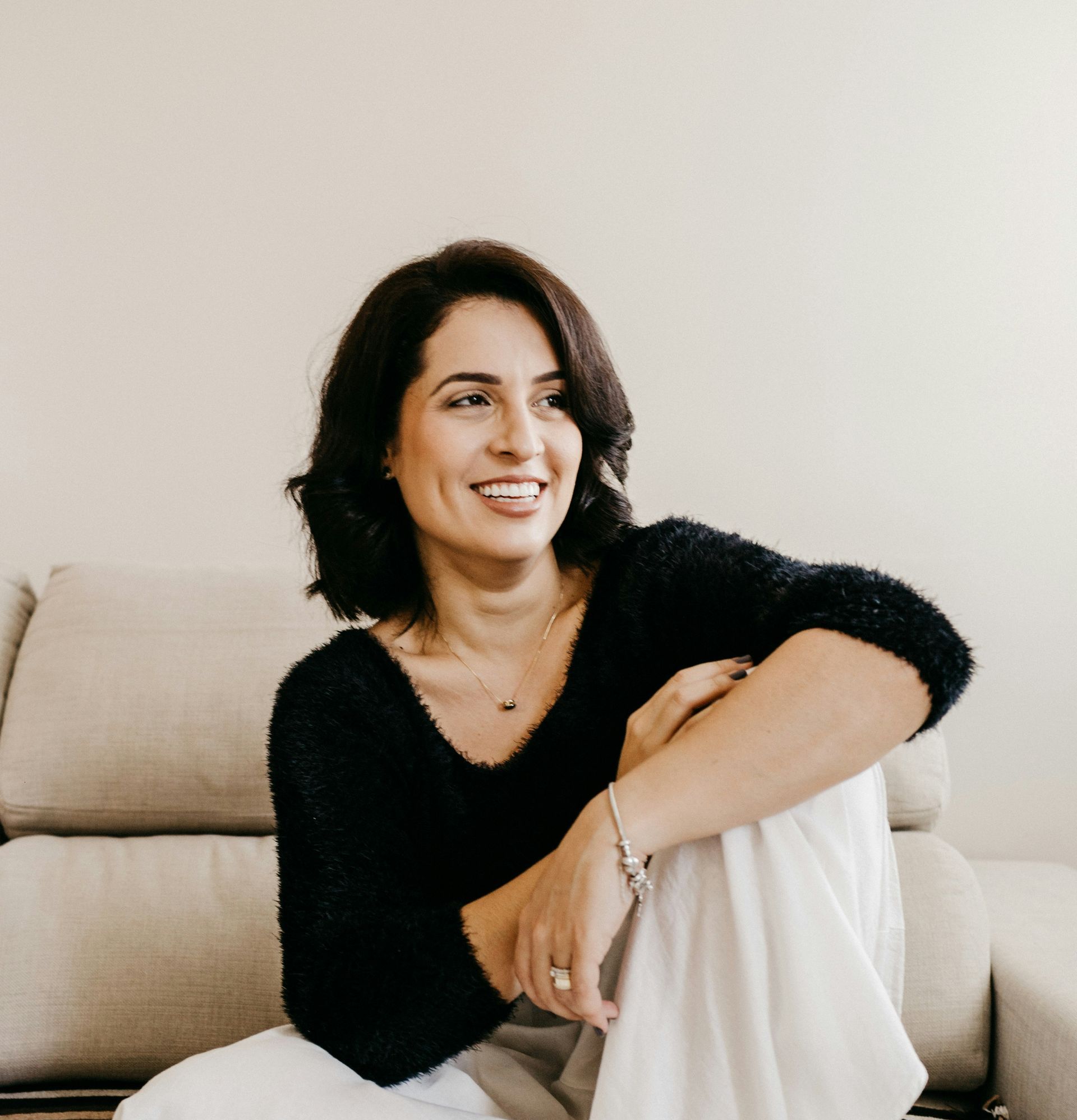 A woman is sitting on a couch with her legs crossed and smiling