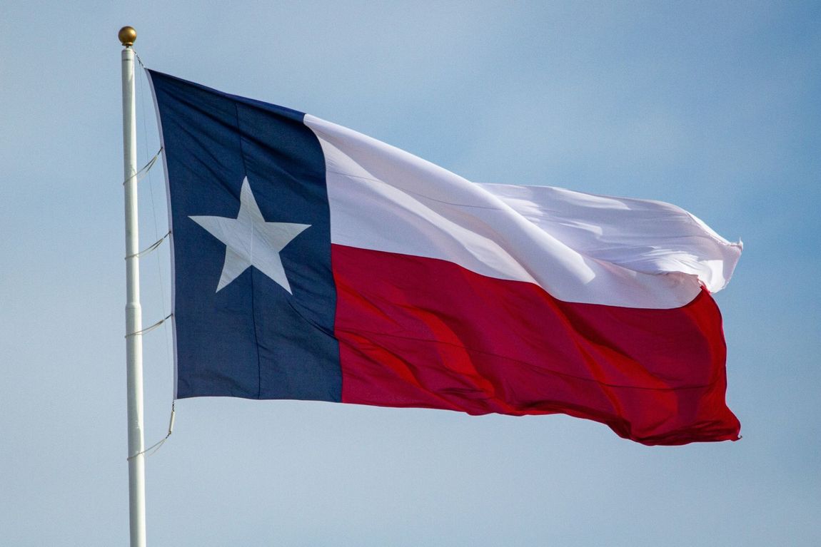 A texas flag is flying in the wind