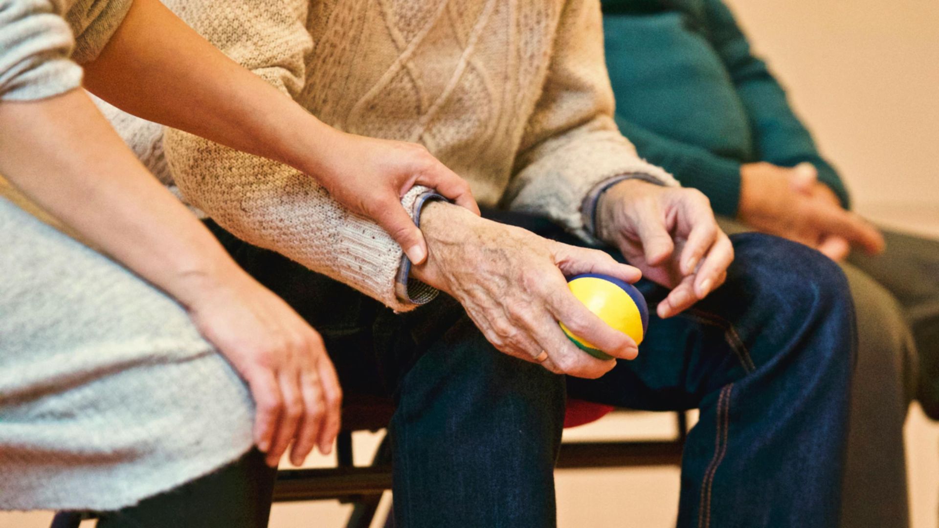 A woman is holding the hand of an elderly man while sitting in a chair.