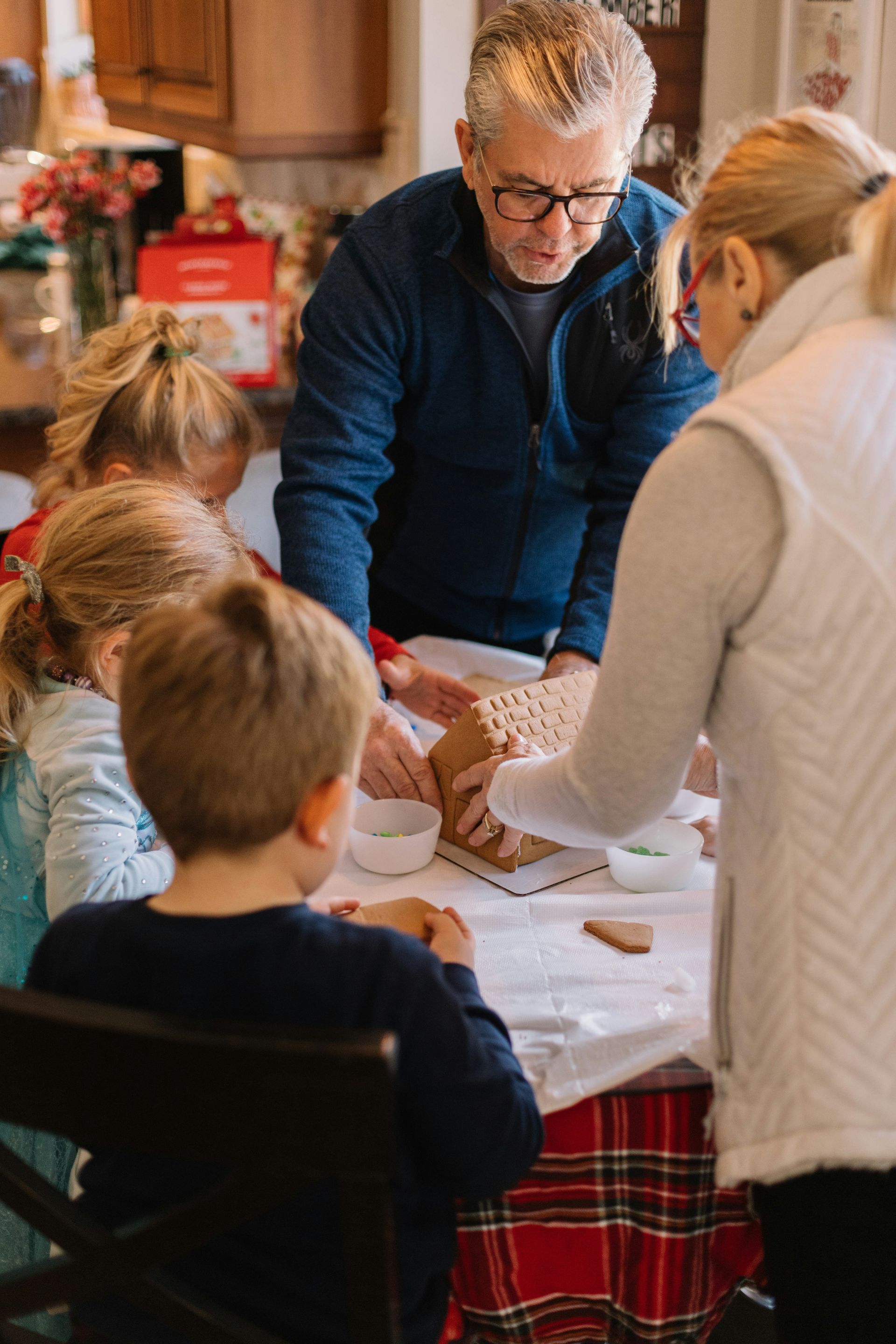 A group of people are sitting around a table making gingerbread houses.