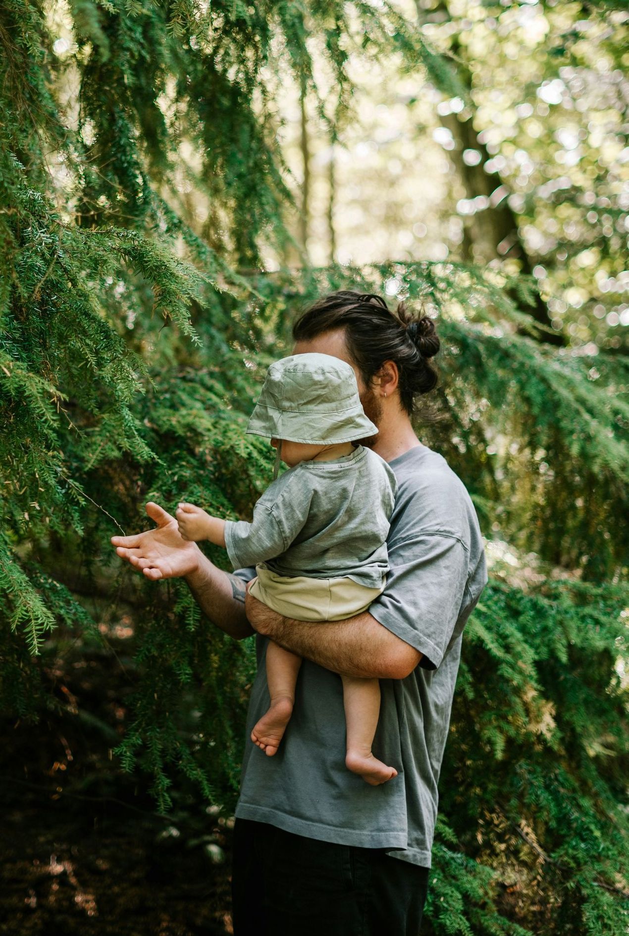 A man is holding a baby in his arms in the woods.