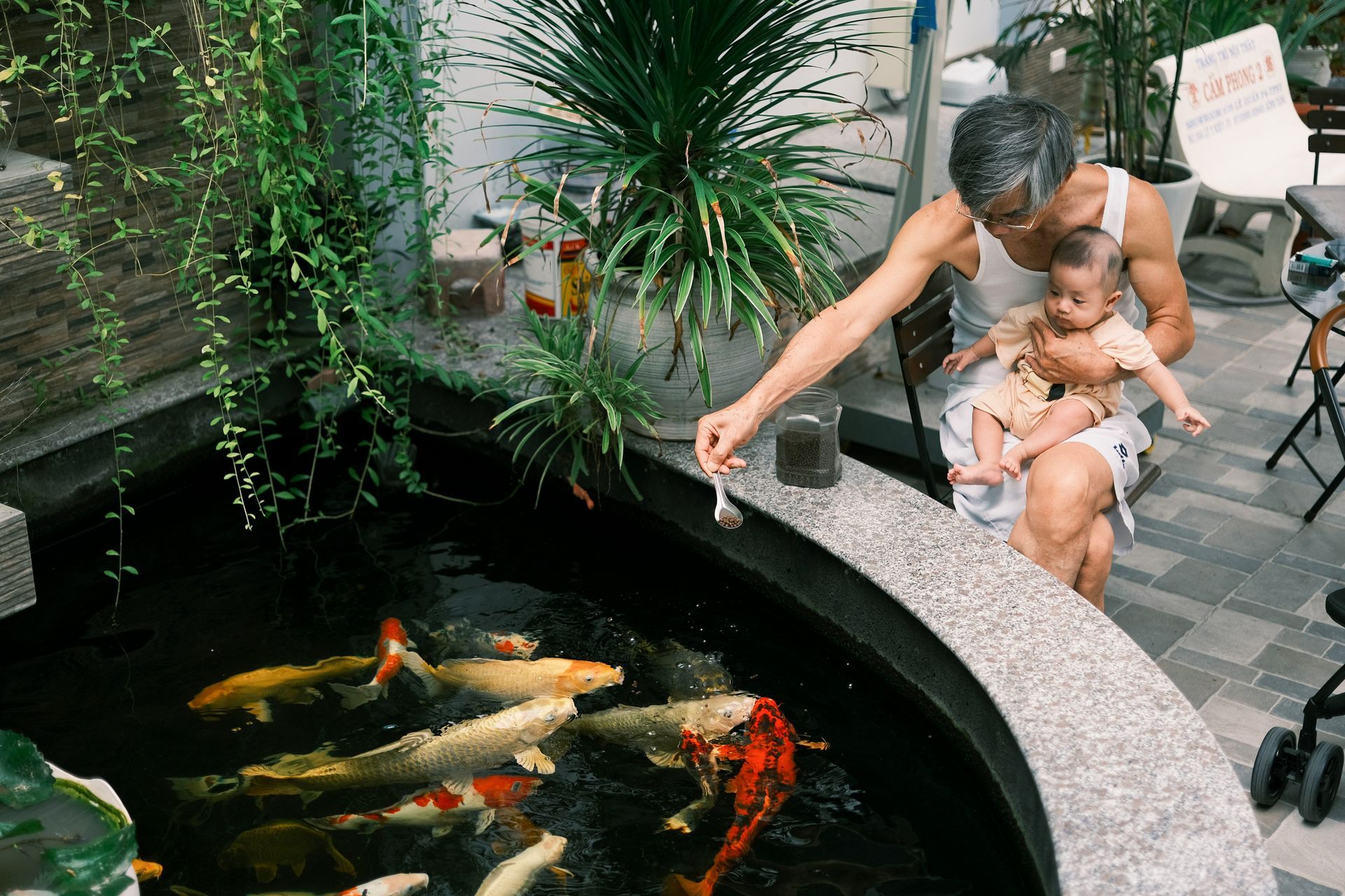 A man is holding a baby and feeding fish in a pond.