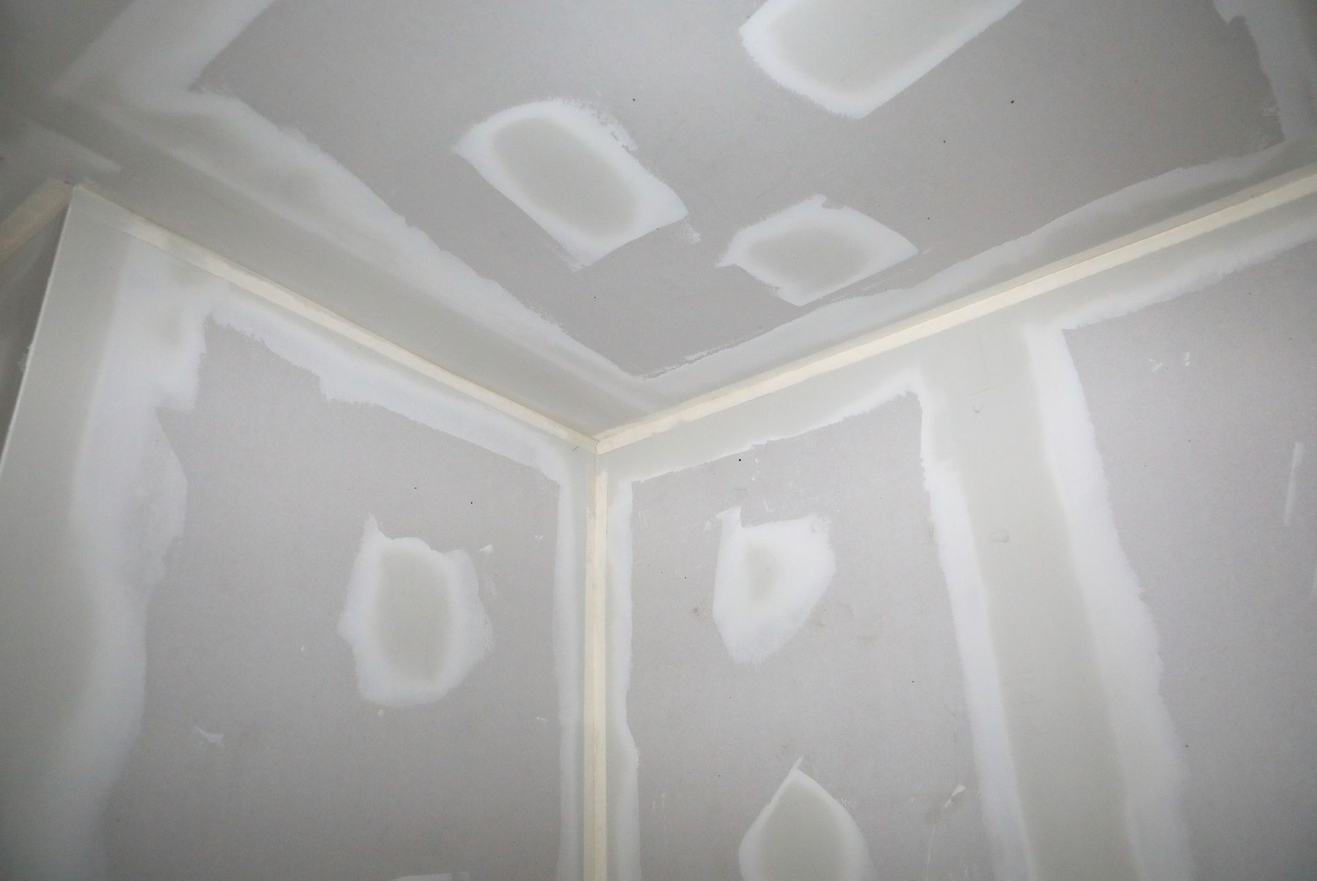 A corner of a room with drywall walls and a ceiling.