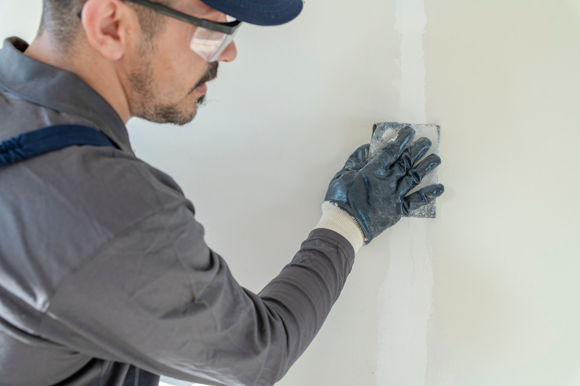 A man wearing safety glasses and gloves is plastering a wall.