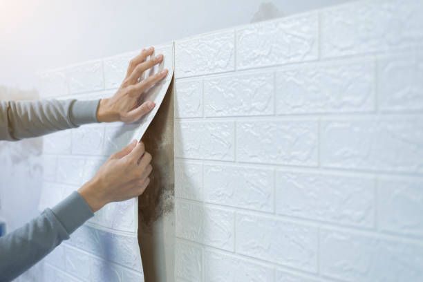 A person is peeling off a piece of wallpaper from a brick wall.