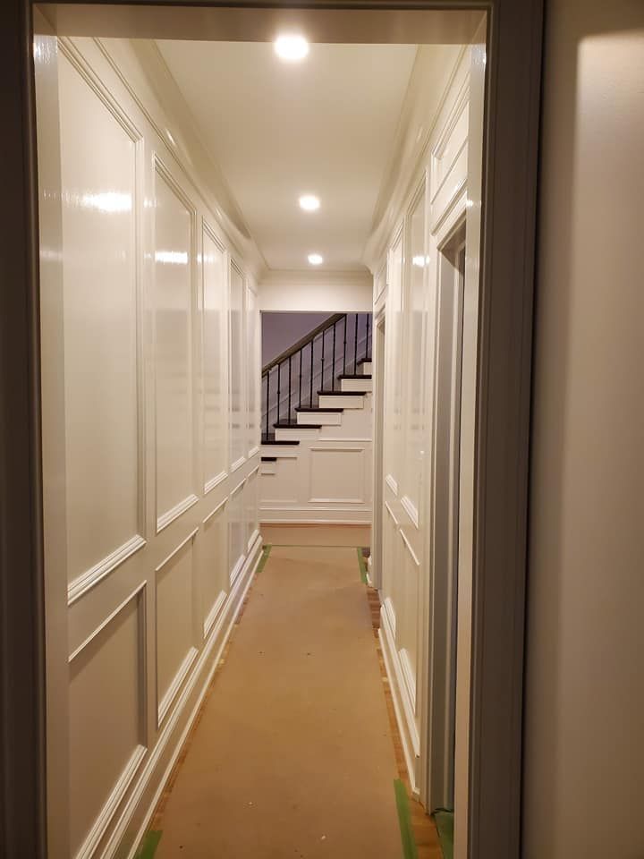 A long hallway with white paneling and stairs in the background.