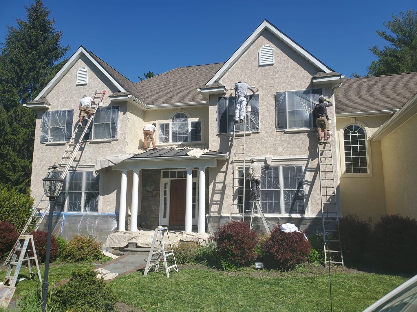 A large house is being painted by several people on ladders