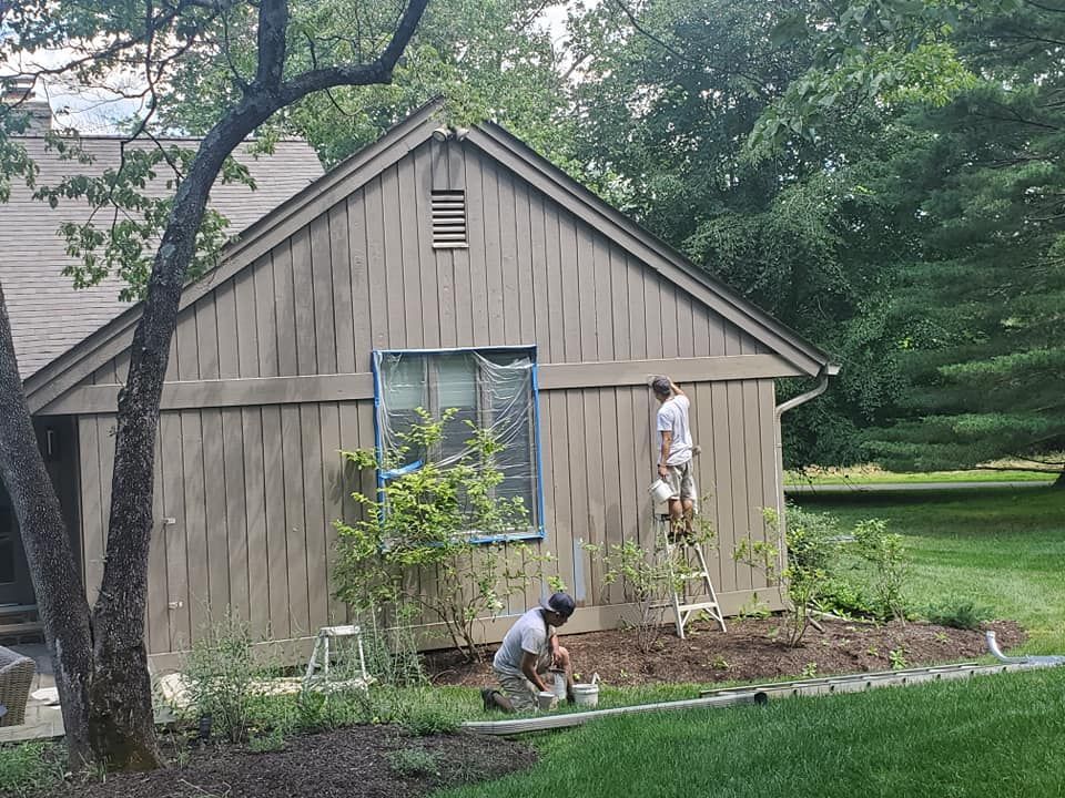 A man on a ladder is painting the side of a house