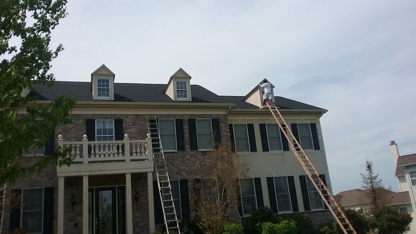 A man on a ladder is painting the roof of a large house.