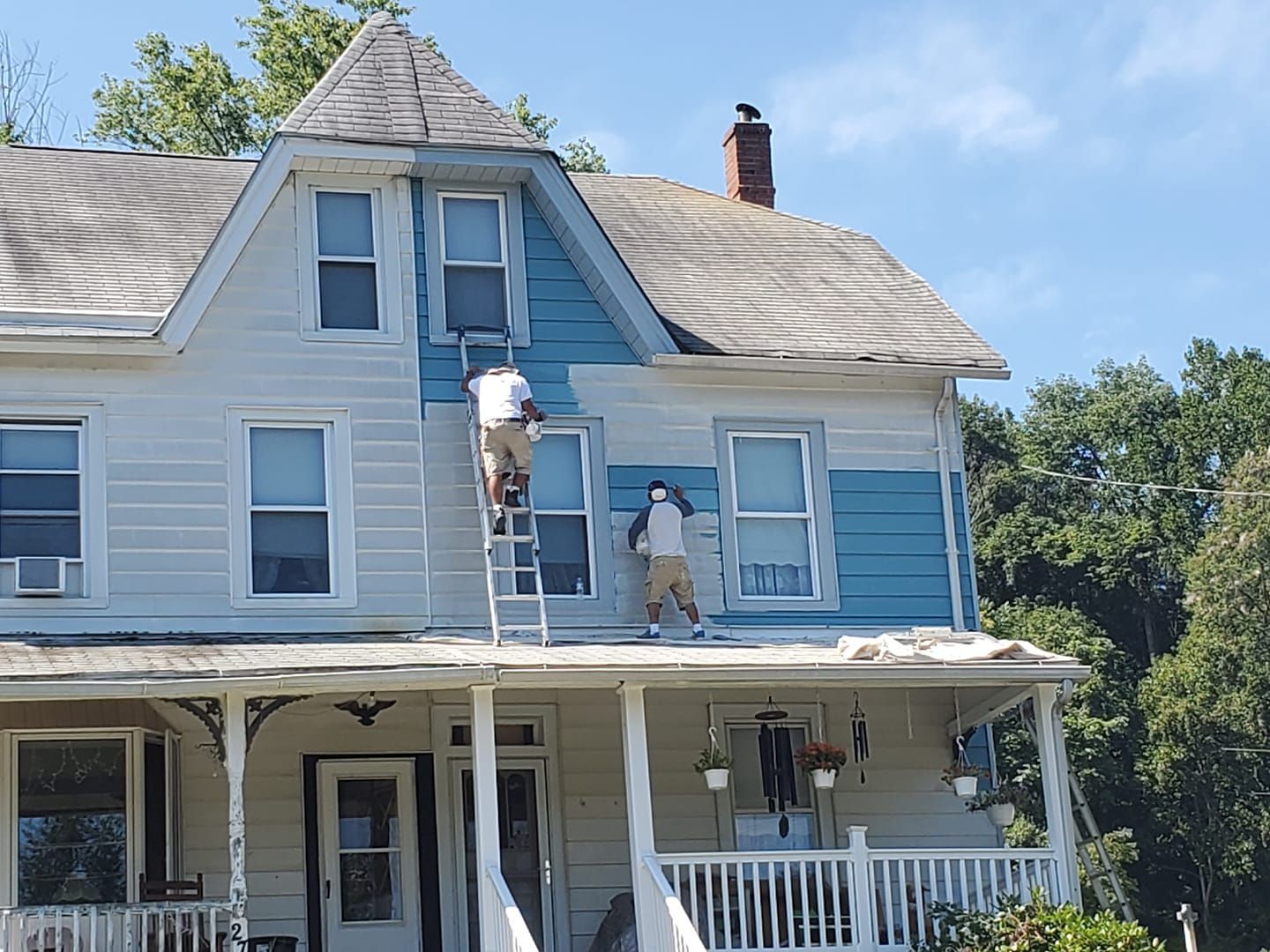 A man on a ladder paints the side of a house