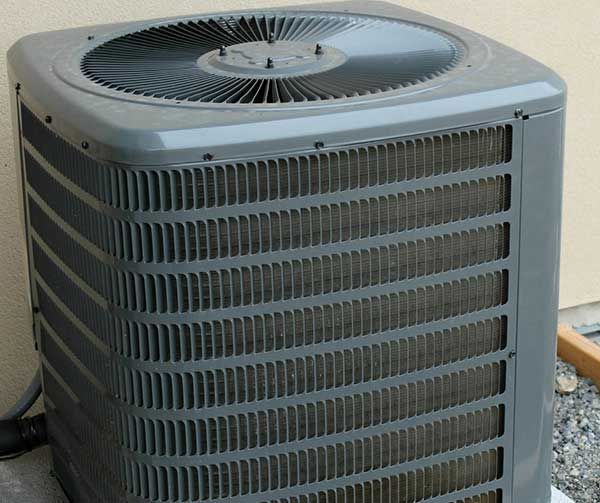 Gray outdoor air conditioning unit beside a wall, with a fan on top and vented sides.