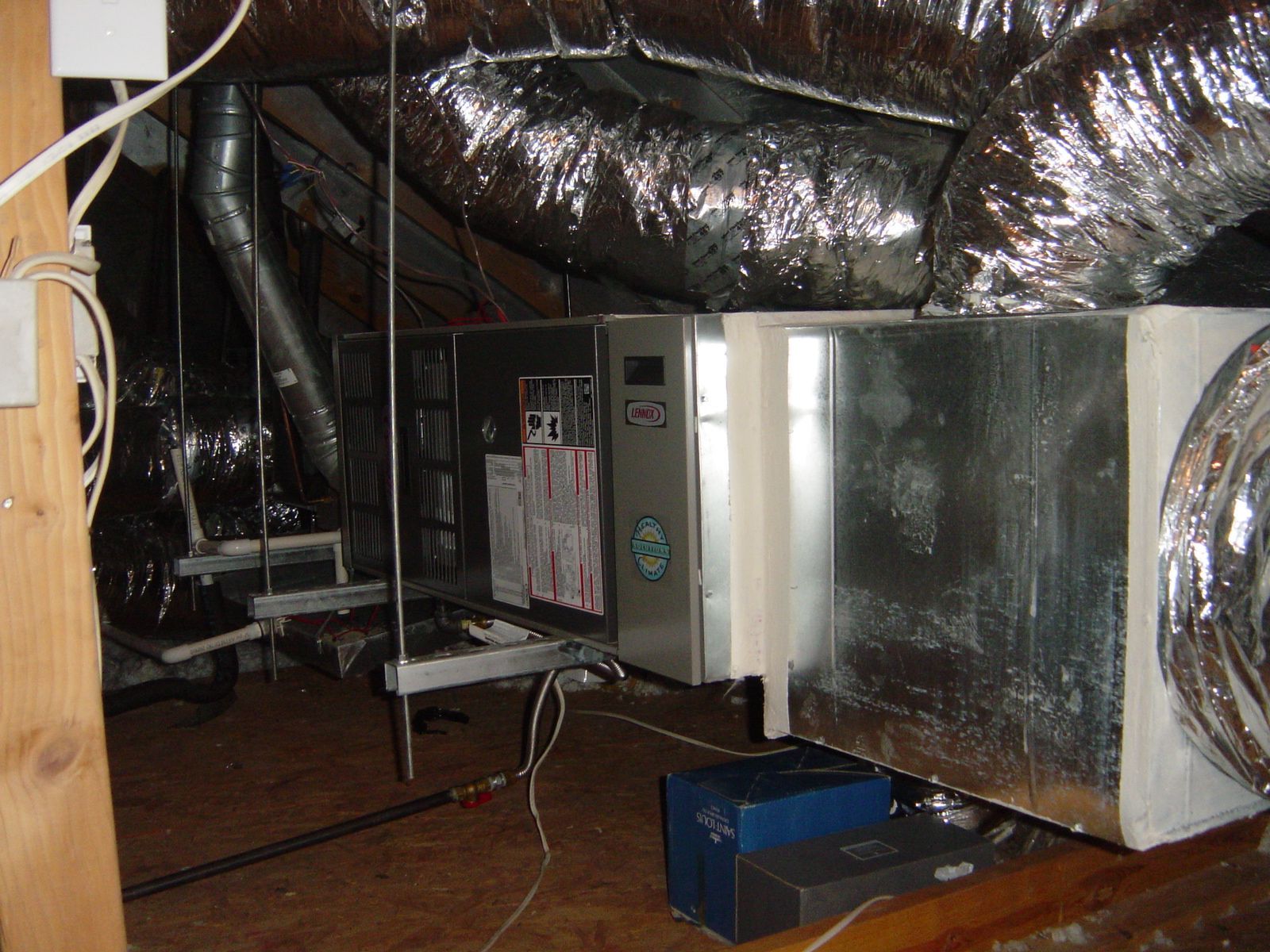 Technician repairing an outdoor HVAC unit beside a brick wall, with tools and hoses on the ground