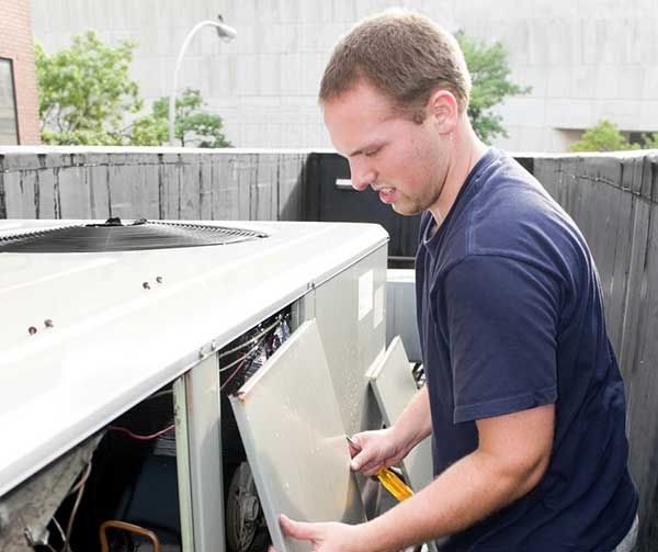 Technician opening an outdoor HVAC unit and inspecting its interior panel