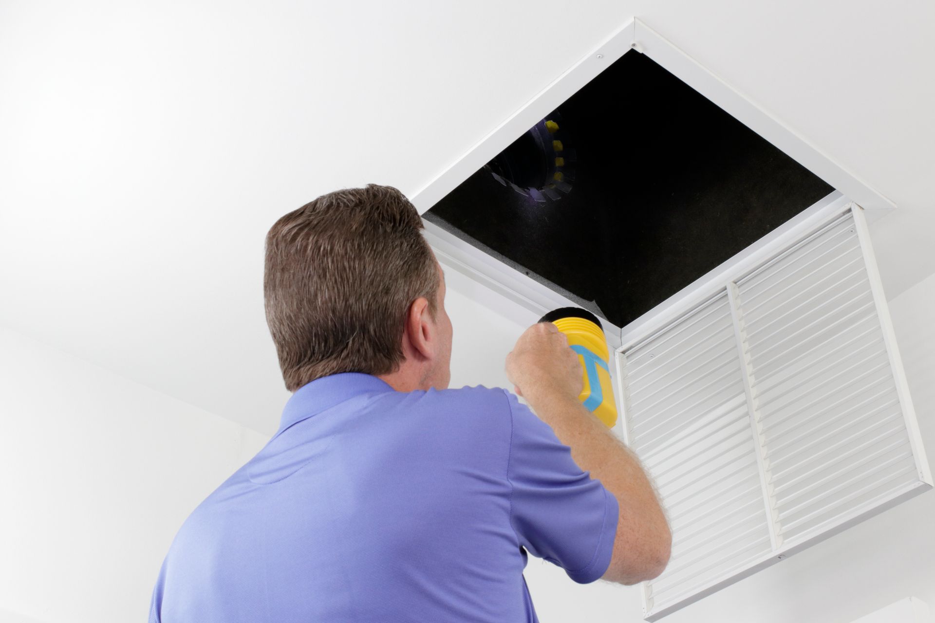 Person cleaning a ceiling vent with a cloth beside an open attic access panel