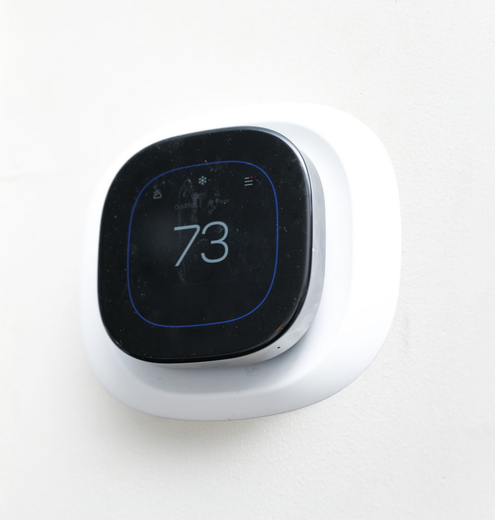 Smart thermostat with black screen showing 73°F on a white wall mount