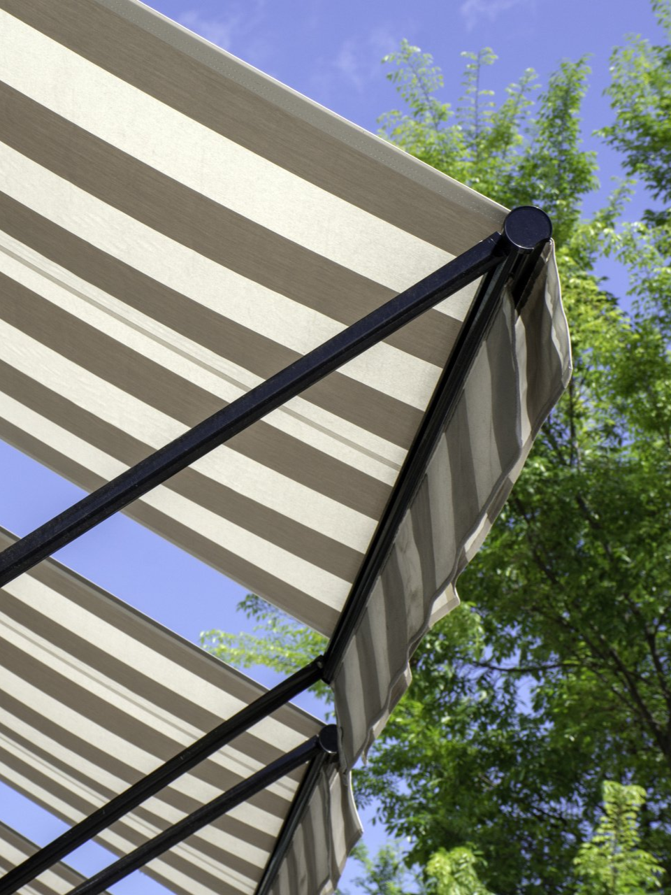 Striped awning with a black frame, blue sky visible, and green trees in the background.