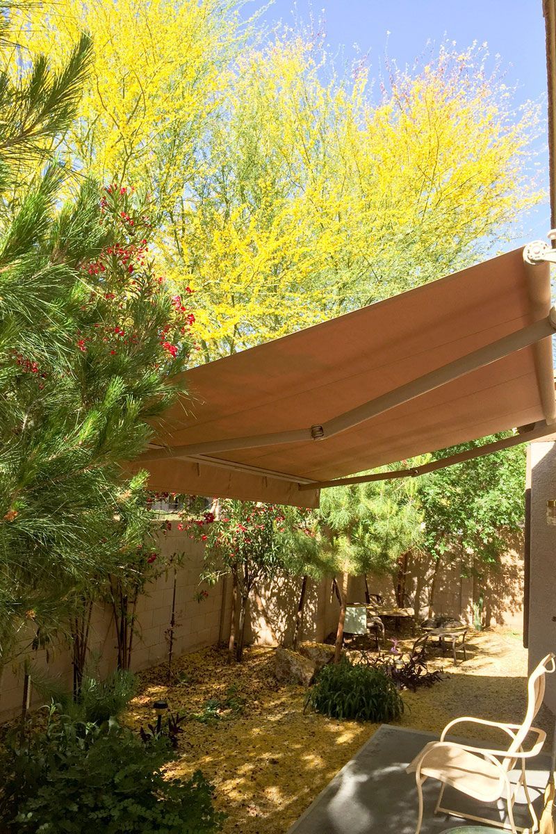 Outdoor kitchen with a grill, awning, and seating near a pool.