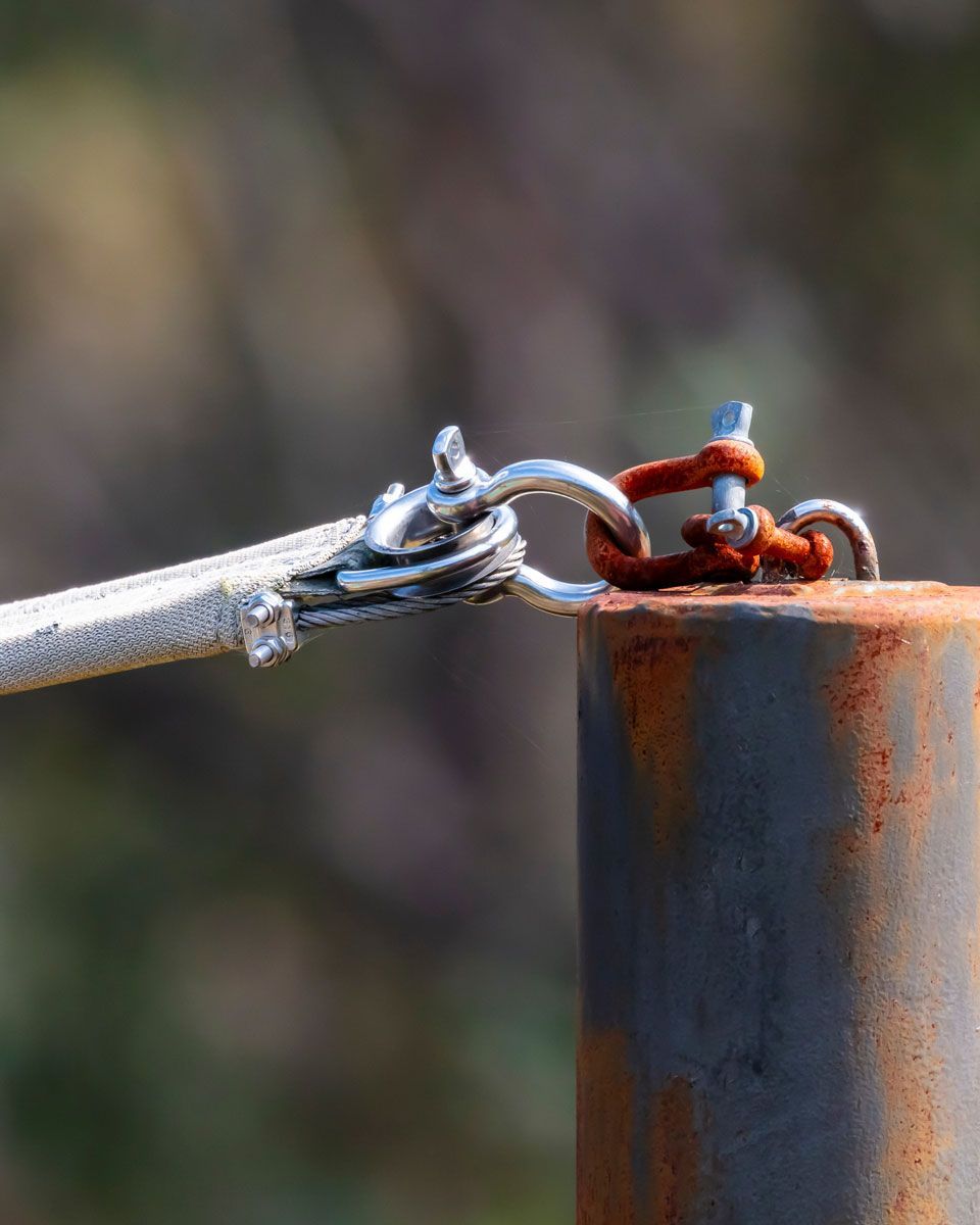 A metal post with a rusty fitting connects to a cable via a chain and connector.
