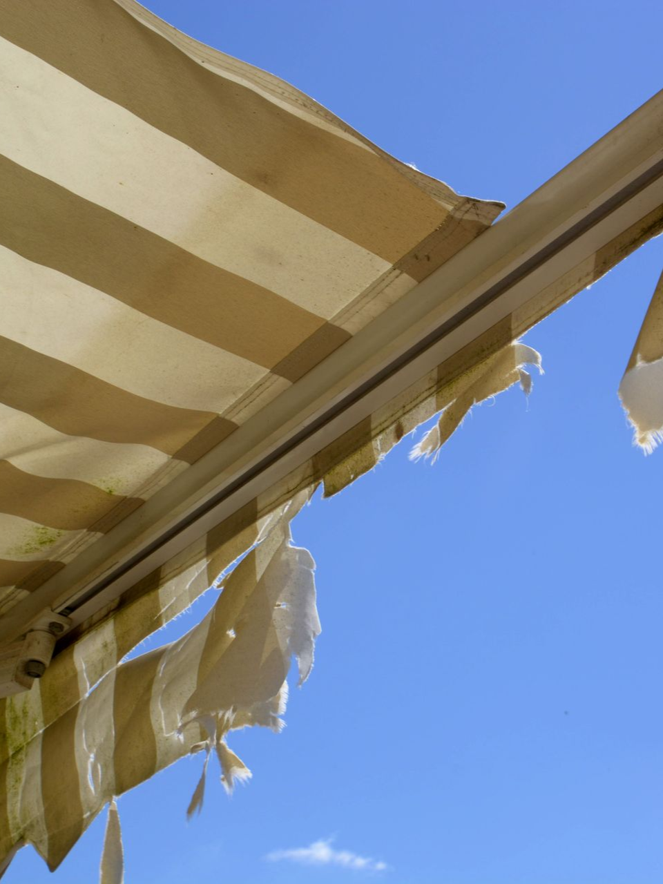Torn, striped awning against a bright blue sky.