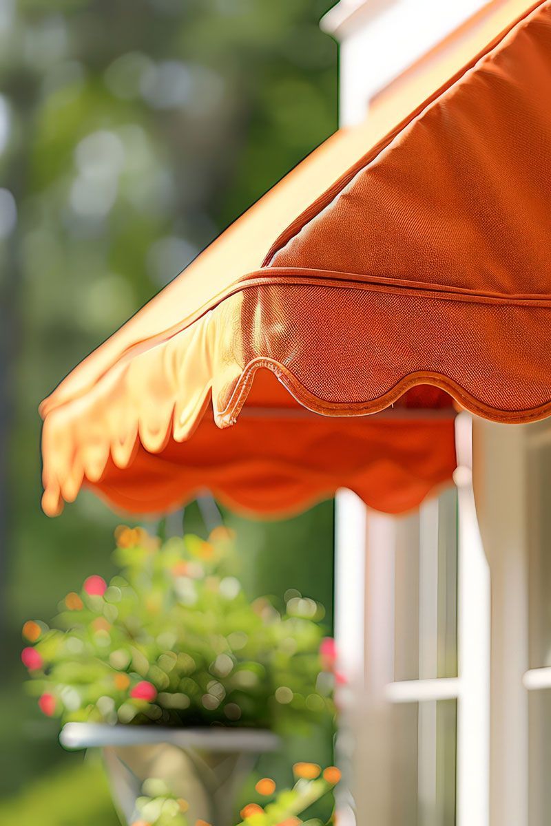 Orange awning over window with scalloped edge, blurred green foliage and flowers in background.