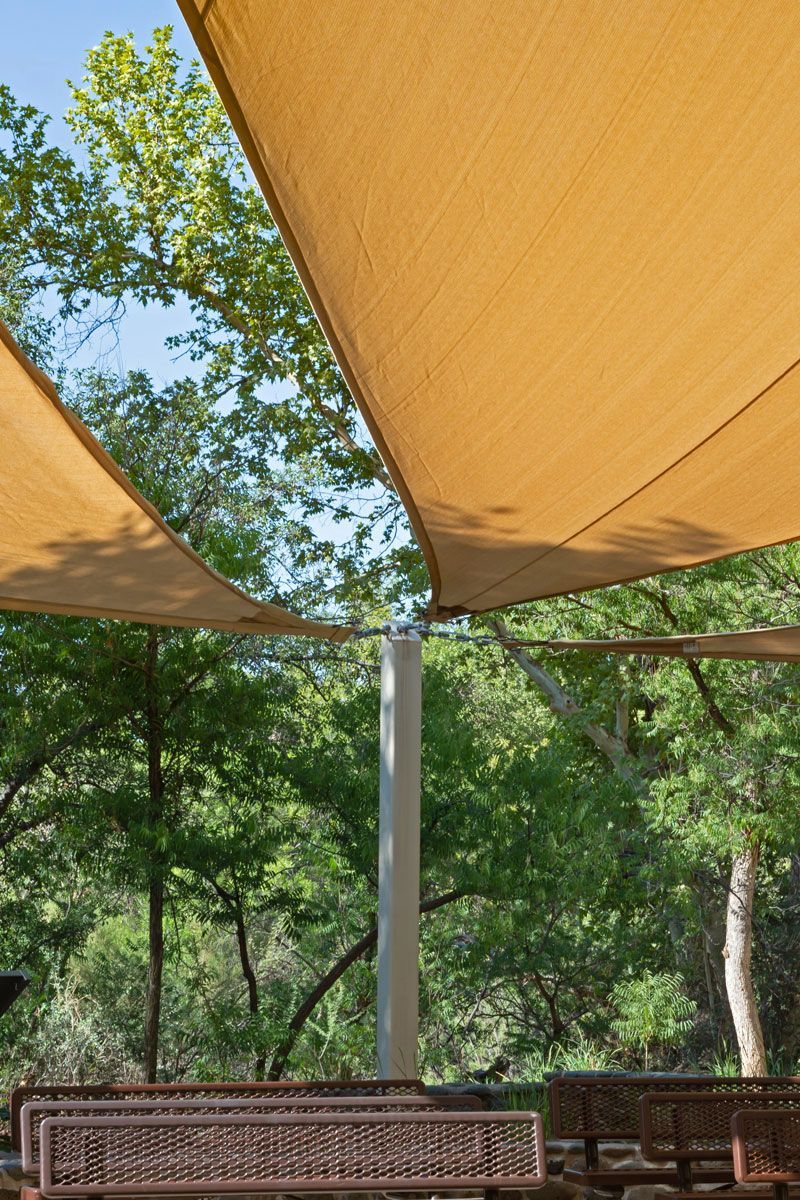 Shade sails over picnic area with bench, trees, and blue sky.