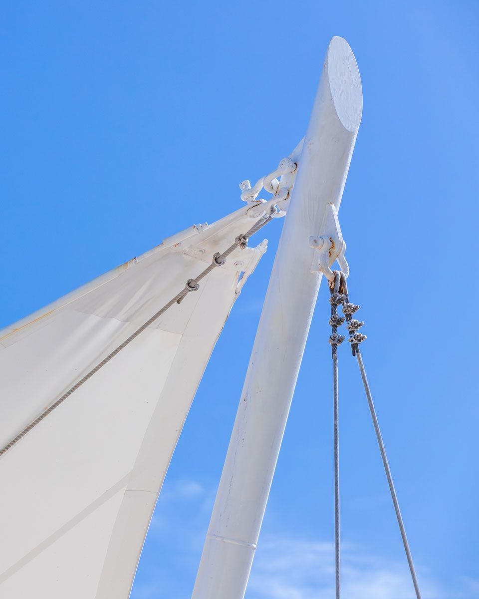 White architectural structure against a bright blue sky; features a curved support, cables, and a white canopy.