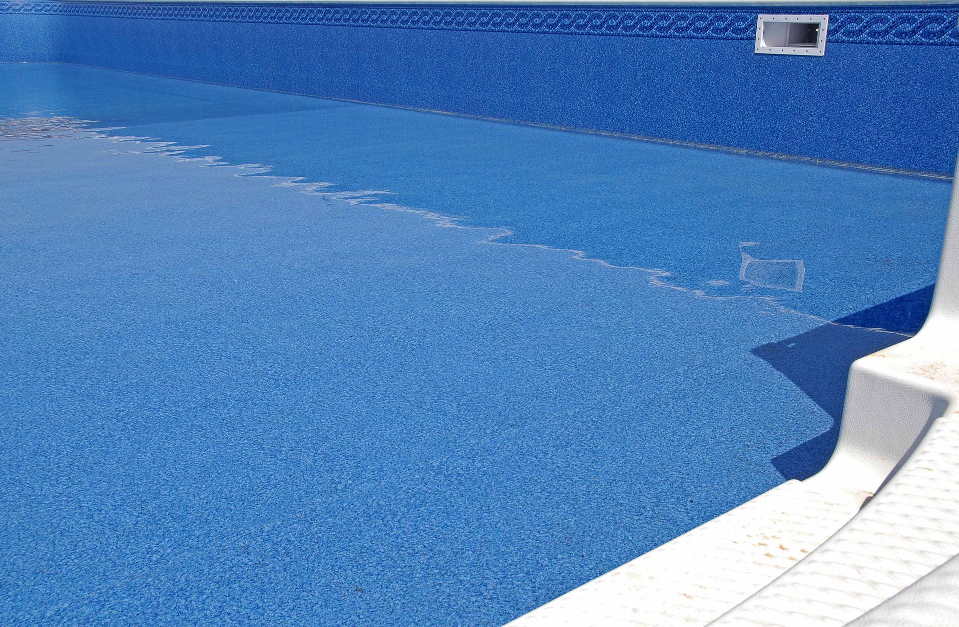 A close up of a swimming pool with blue tiles and steps.
