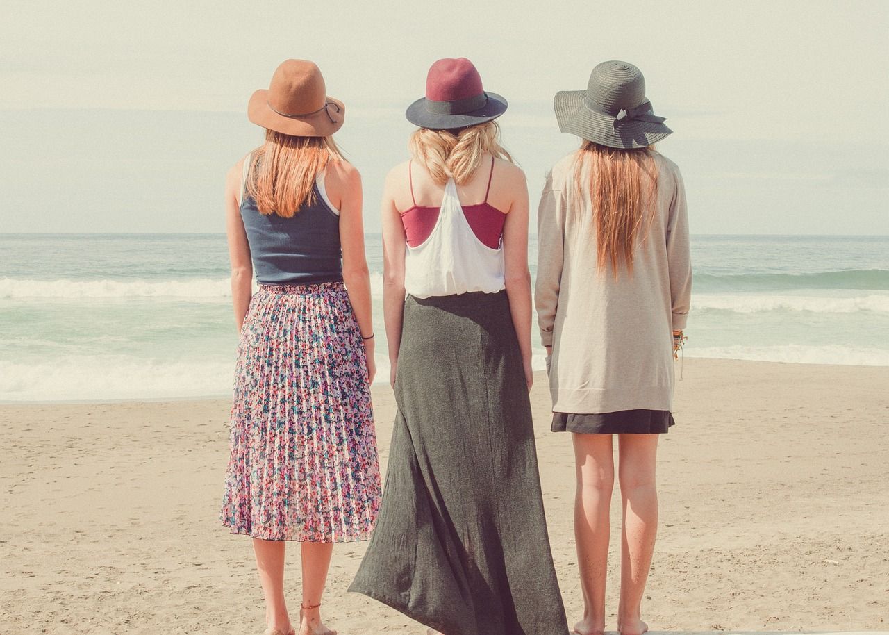 Drei Frauen am Meer mit jeweils einen Sonnenhut. Schauen zu dem Horizont. Symbolisieren Freundschaft