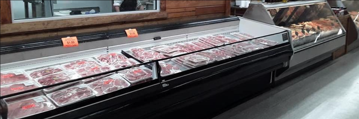 A long, refrigerated glass display case in a supermarket filled with various cuts of packaged raw meat.