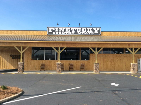 The exterior of Pinetucky Country Meats, a wood-sided building with a sign and a covered porch with rocking chairs.