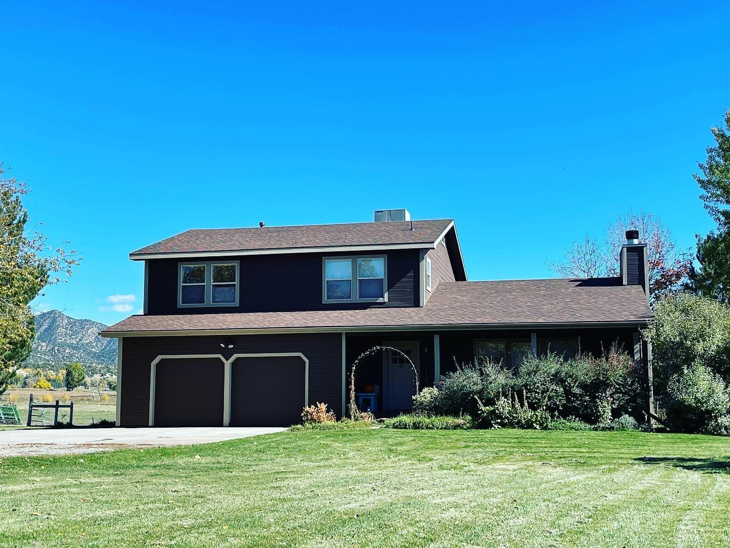 Brown two-story house with a two-car garage under a bright blue sky and green grass.