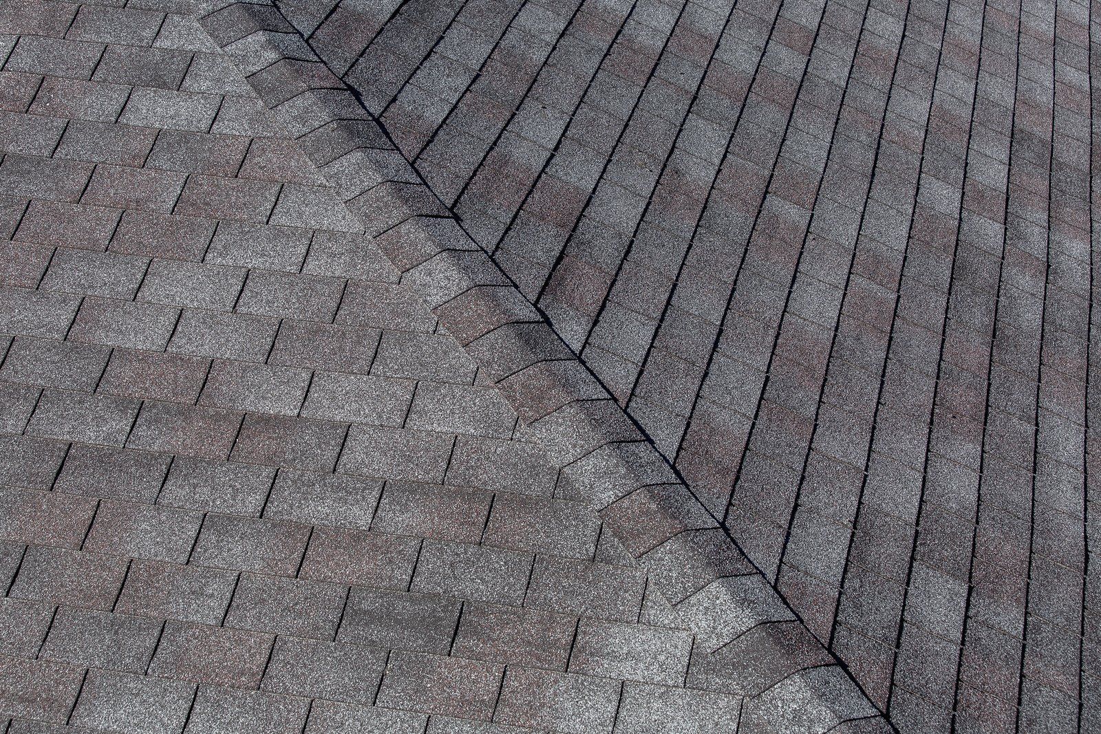 A close-up view of an asphalt shingle roof, showing a diagonal transition where two roof planes meet at a valley.