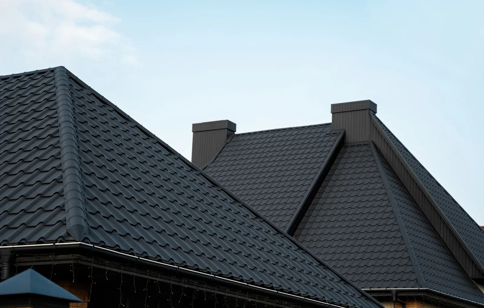 Dark-colored tiled roofs with chimneys against a pale blue sky.