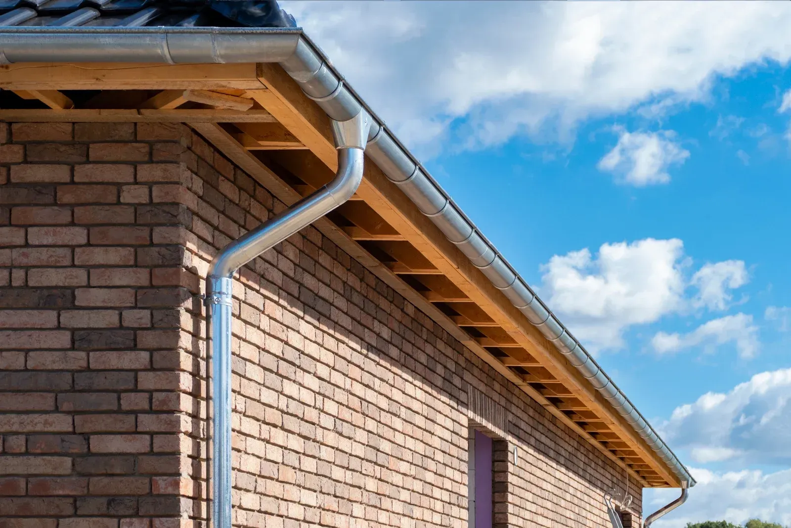Brick building with a metallic rain gutter along the roofline, against a blue sky with clouds.
