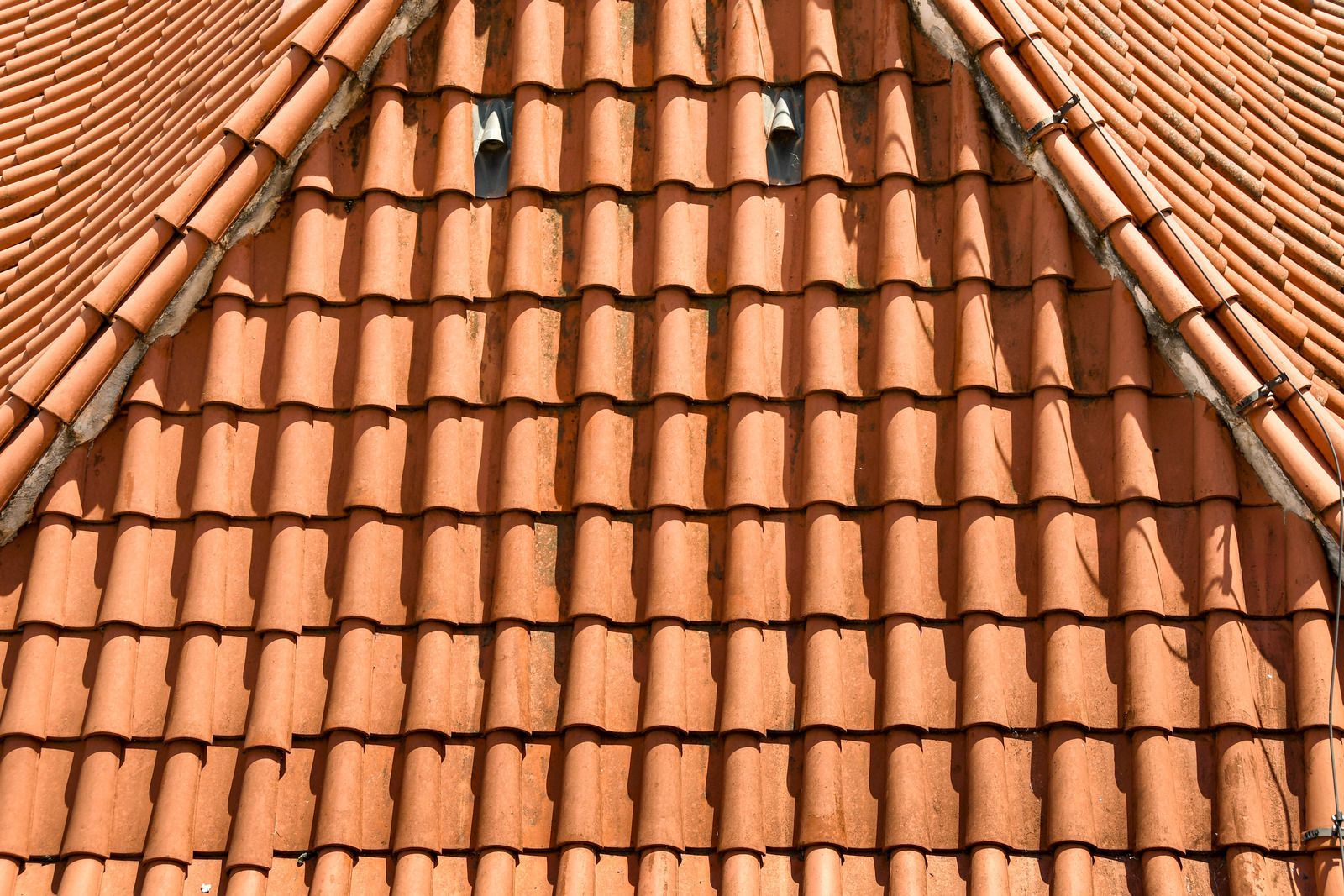 A close-up view of an orange terracotta tiled roof with two small ventilation openings near the peak.