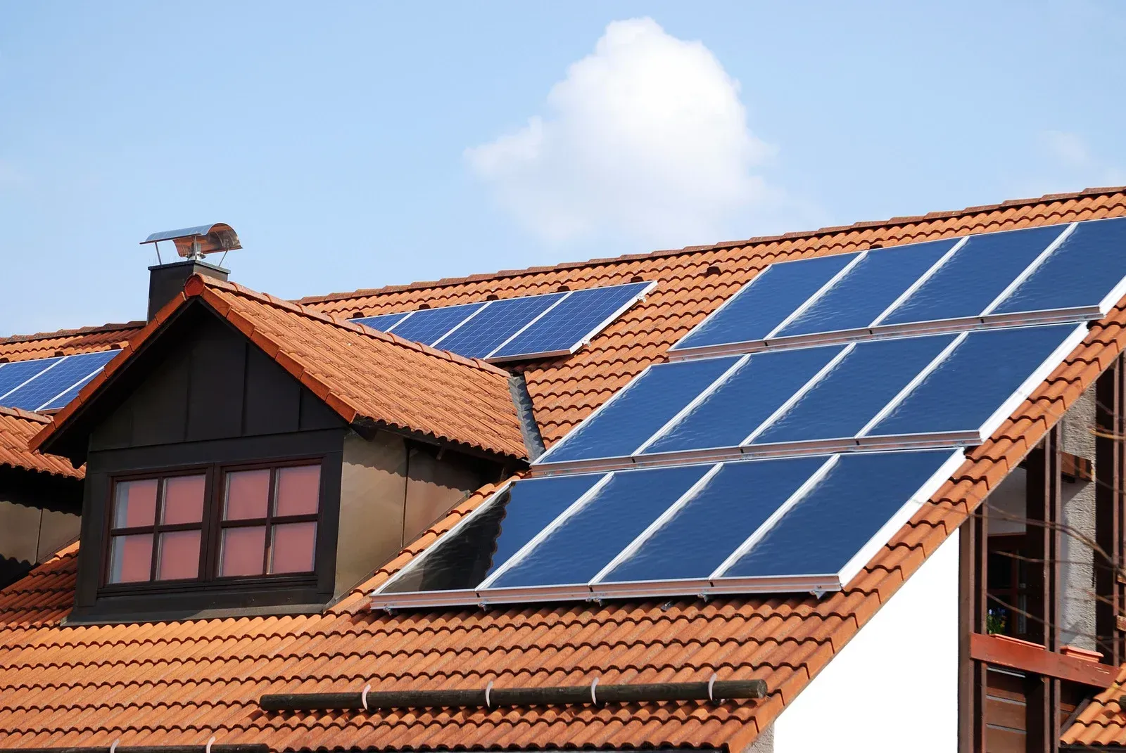 Solar panels on a red tile roof, mounted on a house under a blue sky.