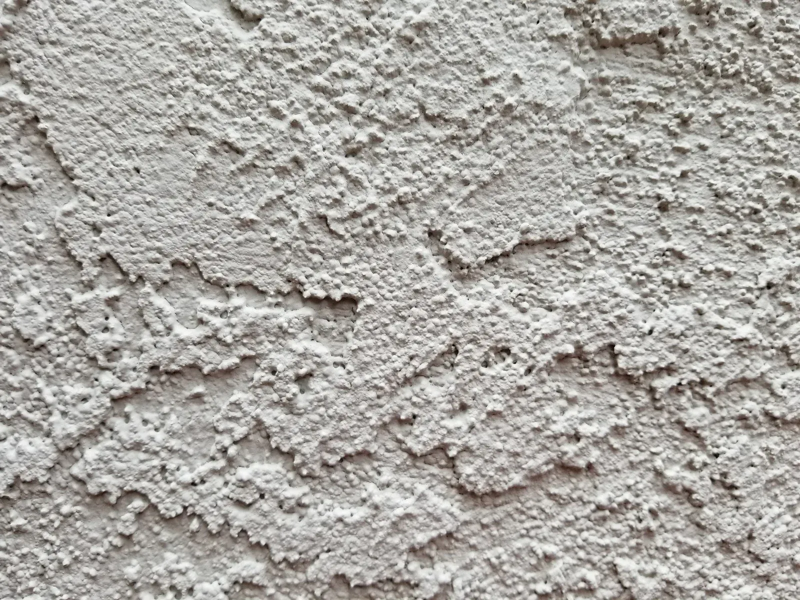 A close-up of a rough, light gray stucco wall texture with an uneven, bumpy surface.